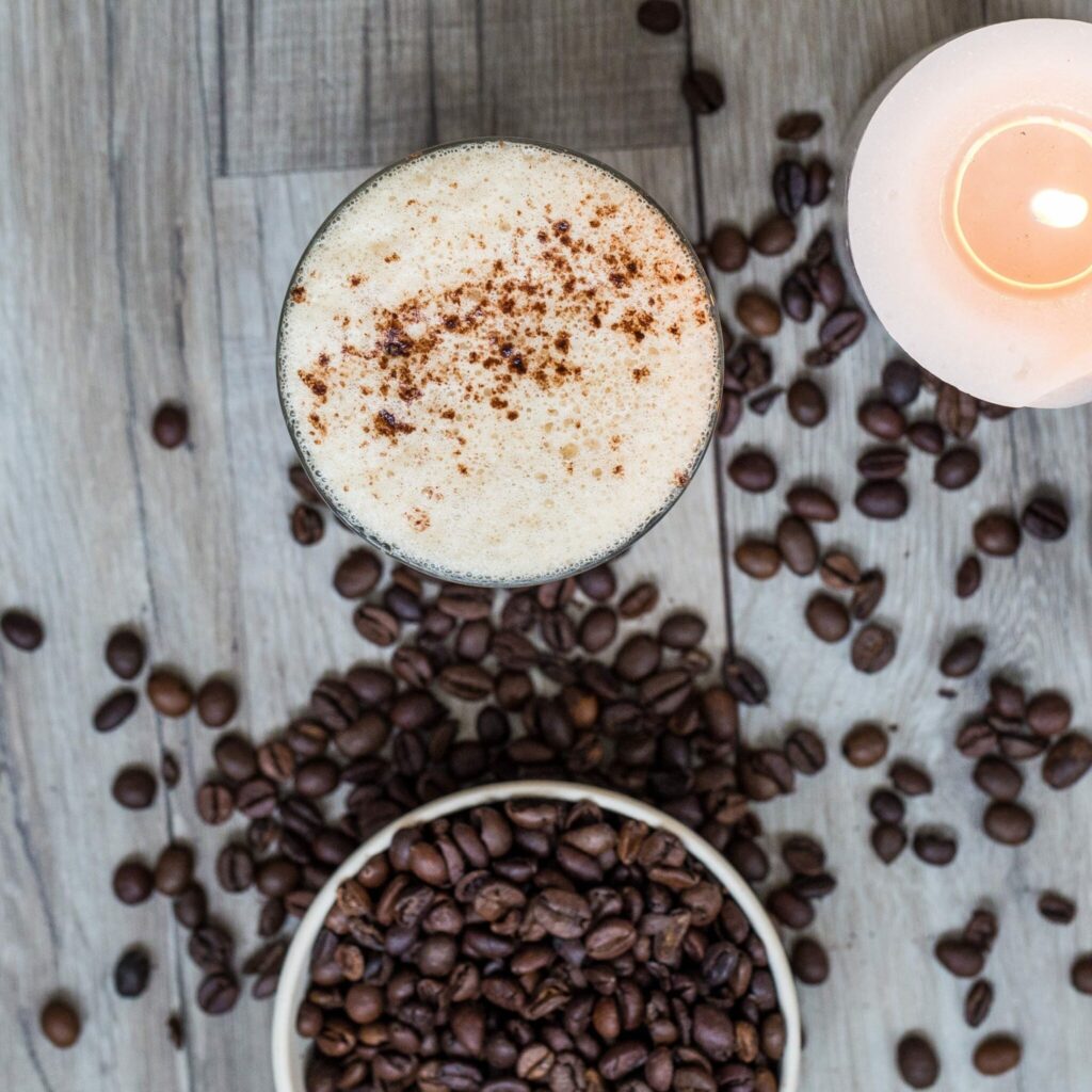 Coffee beans lie next to a hot drink with milk foam, seen from a bird's eye view.
